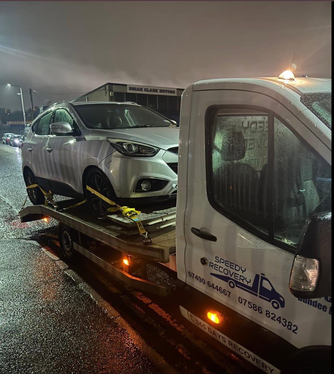 Speedy Recovery flatbed on a night callout in Dundee — amber beacon lit, a car strapped on the bed
